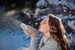 Eine Frau, die Schnee aus ihren handschuhen bläst.