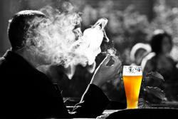 Ein mann sitzt in einer Rauchwolke seiner Zigarette und trinkt Bier.